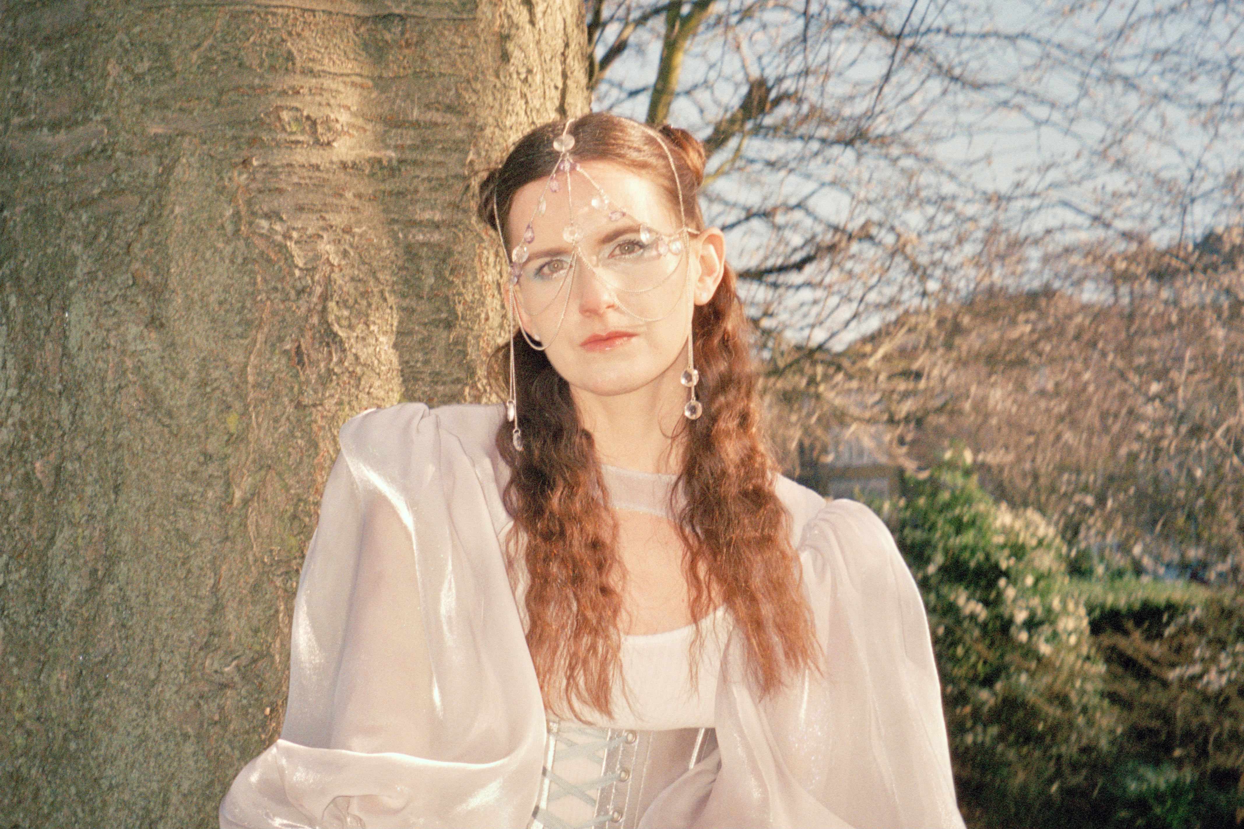 MOLTENO in a pale blue tulle gown looking up past a blossoming tree.