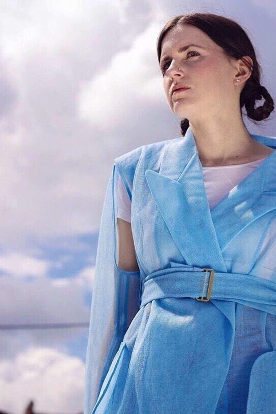 MOLTENO in a sheer pastel blue belted coat against a cloudy sky.